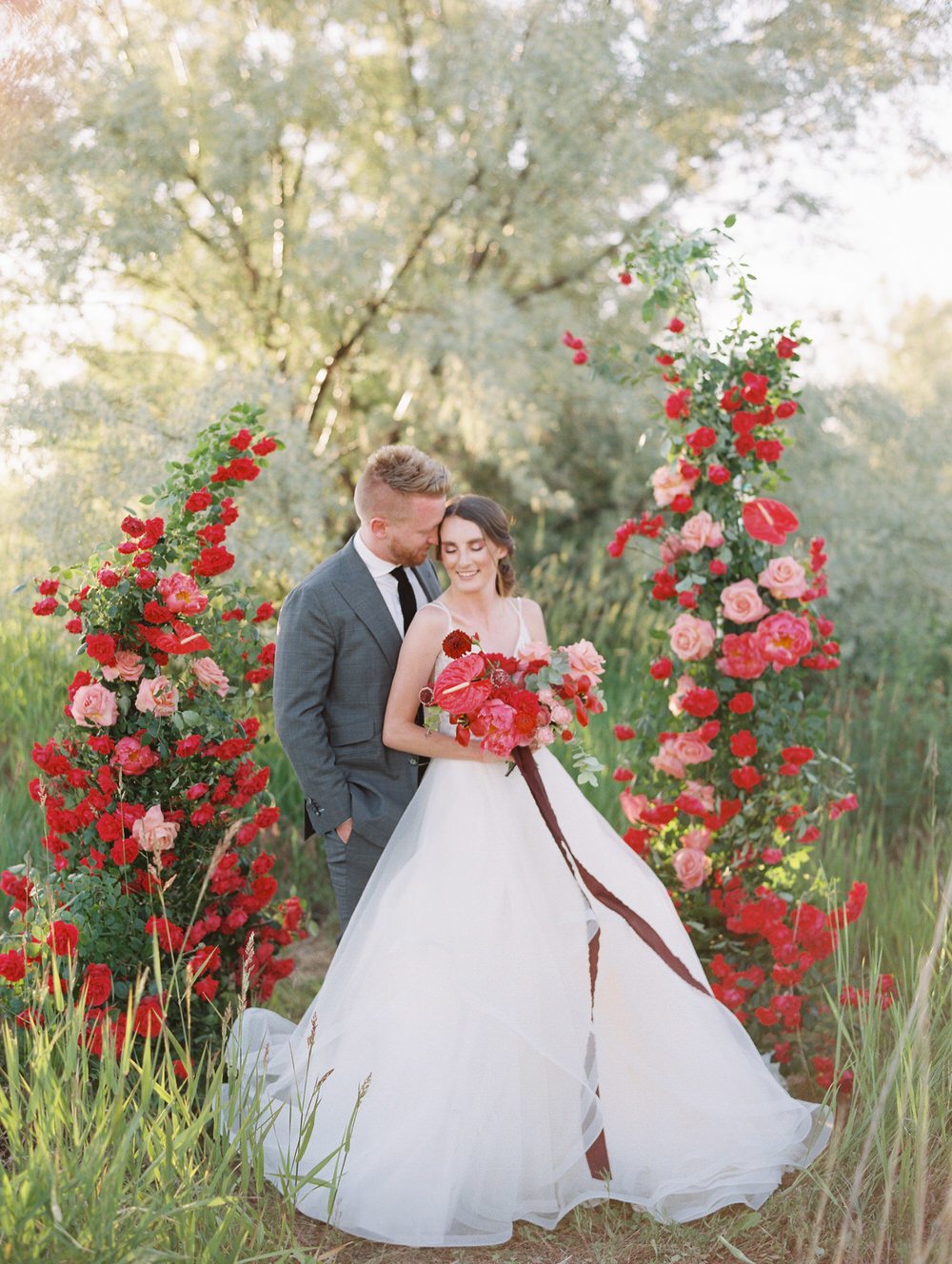 bride and groom surrounded by red roses