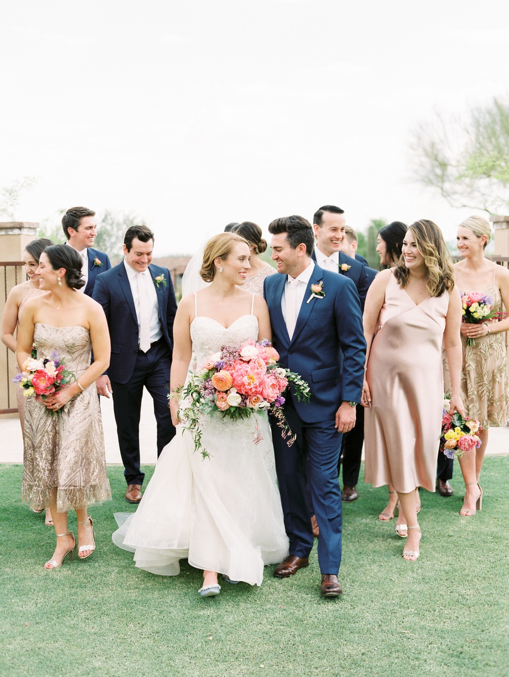 bride and groom smile as they walk with their wedding party behind them