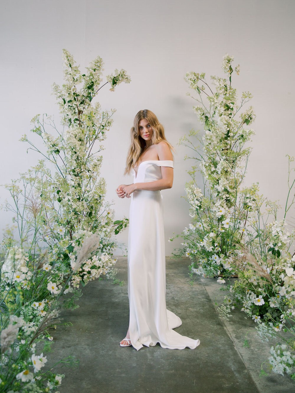 bride standing under a wild flower ceremony arch