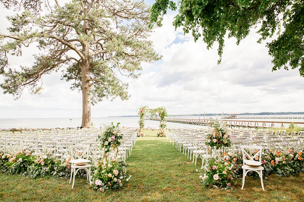riverside wedding ceremony with garden flowers and white chairs