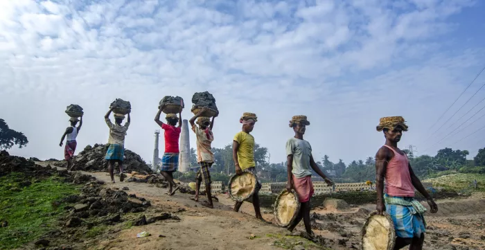 Indian men carry clay and materials to and from a brick kiln.